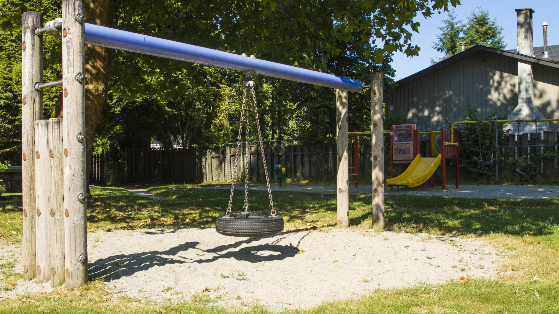 A wood framed swing set with a tire swing over a small patch of sand. There is a slide behind it.